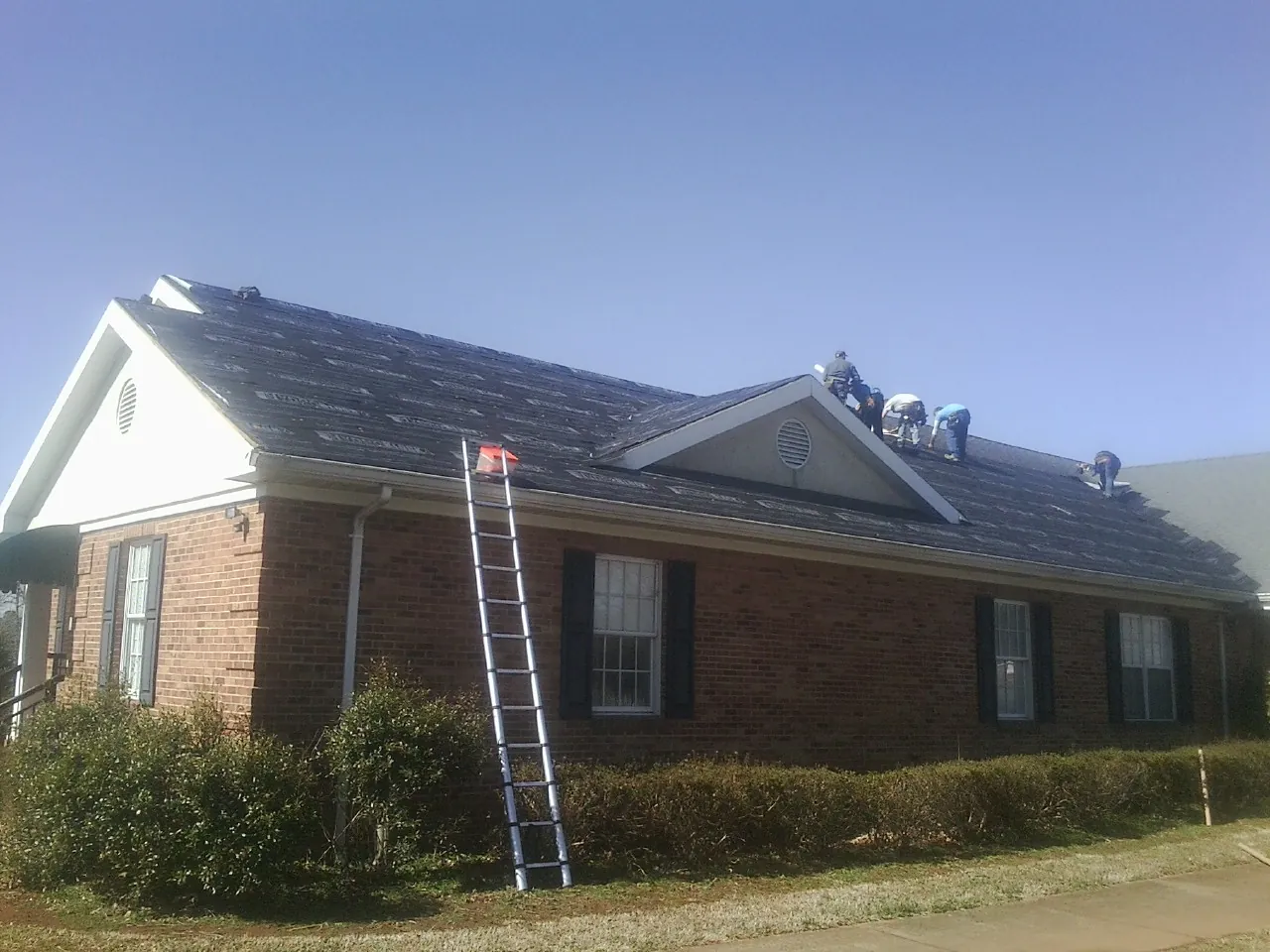 Crew tearing shingles off a brick ranch roof with a ladder set — Emergency Roof Repair work by our crew in Audubon